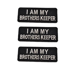 Può includere: Tre toppe rettangolari nere con testo ricamato bianco che recita "I AM MY BROTHERS KEEPER". Le toppe sono disposte verticalmente su uno sfondo bianco.