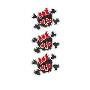 May include: Three identical embroidered patches featuring a black skull with crossed bones behind it. The skull has a red bow on top and two red heart-shaped eyes. The embroidery uses black, white, and red thread to create the detailed design.