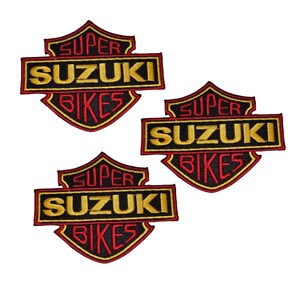 Puede incluir: Tres parches bordados con un diseño de escudo. Cada parche presenta las palabras "SUPER SUZUKI BIKES" en hilo dorado y rojo sobre un fondo negro. Estos parches son probablemente para entusiastas de las motocicletas.