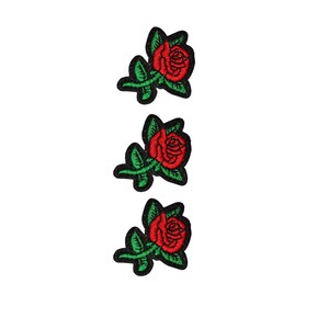 Puede incluir: Tres parches bordados de rosas. Cada parche presenta una rosa roja vibrante con pétalos detallados, hojas verdes y un borde negro. Los parches están dispuestos verticalmente sobre un fondo blanco.