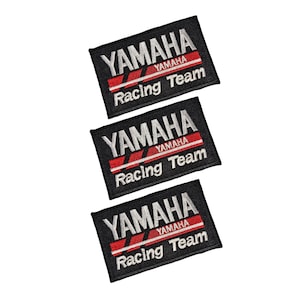 May include: Three black embroidered Yamaha Racing Team patches. Each patch displays the Yamaha logo in white, a red stripe, and the words "Racing Team" in white.