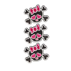 Può includere: Tre toppe ricamate identiche con un design a teschio nero, un fiocco rosa sulla parte superiore e occhi rosa a forma di cuore. Il teschio è posizionato sopra due ossa incrociate, il tutto bordato con filo bianco su uno sfondo nero.