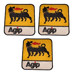 May include: Three embroidered Agip logo patches. Each patch features a yellow background with a black, three-legged dog-like creature breathing red flames. The word "Agip" is embroidered in black on a white rectangular border.