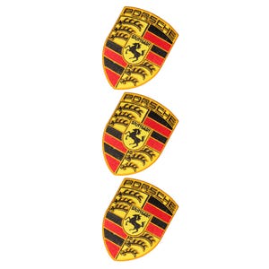 Puede incluir: Tres parches bordados idénticos con el logotipo del escudo de Porsche. Cada parche en forma de escudo muestra la palabra PORSCHE en la parte superior, un caballo negro central, el texto STUTTGART y franjas rojas y negras alternas con detalles dorados.