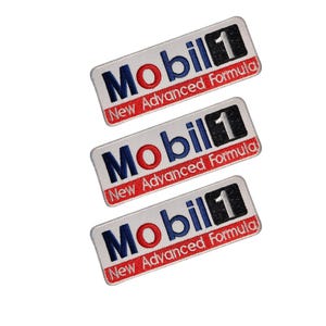 Puede incluir: Tres parches rectangulares con el logotipo de Mobil 1. El logotipo presenta la palabra "Mobil" en azul, el número "1" en negro y el texto "New Advanced Formula" en rojo, sobre un fondo blanco.