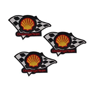 May include: Three embroidered patches with a black and white chequered flag design, a yellow seashell emblem, and the red text "Challenge Team". The patches are set against a white backdrop.