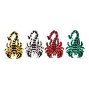 May include: Four embroidered scorpion patches arranged in a horizontal row. Each patch features a black base with a distinct colored outline and segmented body detail in metallic gold, silver, red, and teal green thread respectively.