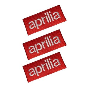 Könnte beinhalten: Drei rote, rechteckige Aufnäher mit dem Wort "aprilia" in Weiß gestickt. Die Aufnäher sind diagonal vor einem weißen Hintergrund angeordnet. Die Aufnäher sind wahrscheinlich für Kleidung oder Accessoires.