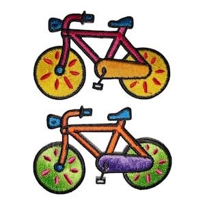 May include: Two embroidered bicycle patches. One bicycle is pink, yellow, and orange, with a blue seat and handlebars. The other bicycle is orange, green, and purple, with a blue seat and handlebars. Both have black outlines.