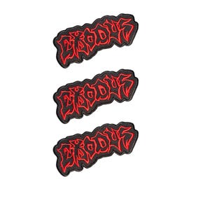 Puede incluir: Tres parches bordados idénticos que muestran la palabra EXODUS en una fuente roja estilizada y dentada con un borde negro grueso. Cada parche tiene una forma irregular distinta que sigue el contorno de las letras, creando un efecto visual.