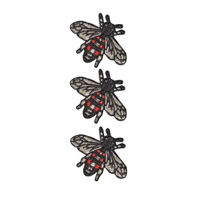 May include: Three identical embroidered bee patches arranged vertically. Each bee features a black head and thorax, with wings in shades of grey and white. The abdomen is striped with black and vibrant red bands, creating a detailed insect design.