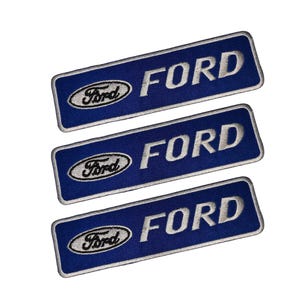Puede incluir: Tres parches rectangulares azules bordados con la palabra "FORD" en letras blancas. Cada parche tiene un borde blanco y el logotipo de Ford en la esquina superior izquierda. Los parches están dispuestos en diagonal.