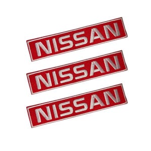 May include: Three embroidered patches featuring the word "NISSAN" in white lettering on a red rectangular base. The patches are set diagonally against a white backdrop.