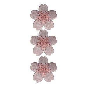 Könnte beinhalten: Drei gestickte Blumenaufnäher in einer Reihe. Jeder Aufnäher hat ein fünfblättriges Design mit hellrosa Außenbereich und einem dunkleren rosa Zentrum. Die Aufnäher sind wahrscheinlich für dekorative Zwecke gedacht, wie z. B. zum Verzieren von Kleidung oder Accessoires.