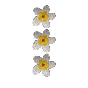 Op de afbeelding: Drie geborduurde bloemvlekken. Elke patch heeft een witte, vijfpuntige bloem met een gele kern en een rode stip in het midden. De patches zijn verticaal gerangschikt tegen een witte achtergrond.