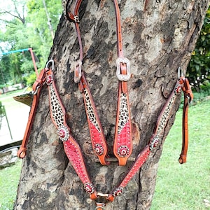 May include: A brown leather horse bridle with a leopard print design and red accents. The bridle features silver buckles and decorative red jewels. The leather is a rich brown color, and the overall design is ornate and detailed.