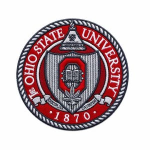 Puede incluir: Un parche bordado circular que presenta el sello de la Universidad Estatal de Ohio en rojo, blanco y gris. El diseño incluye un escudo central con un libro abierto, una hoja, el texto OHIO STATE UNIVERSITY y el año 1870 con un borde de cuerda.