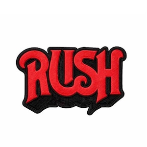 May include: A fabric patch featuring the word RUSH in bold red lettering with a thick black outline and a black drop shadow effect. The design is embroidered with a textured surface and defined edges, creating a distinct graphic logo appearance.