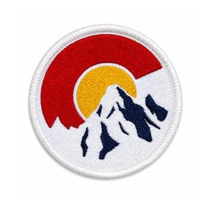 May include: A circular embroidered patch featuring a white background with a red crescent shape at the top, a yellow sun circle in the center, and a dark blue mountain peak silhouette at the bottom, all enclosed by a white stitched border.