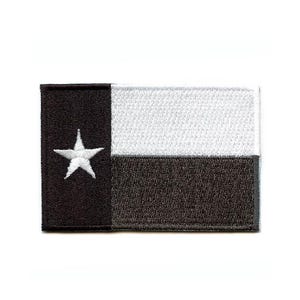 May include: A rectangular embroidered patch featuring the Texas state flag design. The patch has a vertical black stripe on the left side containing a single white star, and horizontal white and black stripes on the right side with a stitched border.