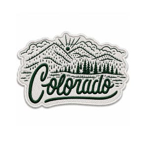 Puede incluir: Un parche bordado con fondo blanco que muestra un paisaje de montañas y bosque en color verde oscuro. La palabra Colorado está bordada en cursiva verde oscuro en la parte inferior del diseño, con un sol estilizado en la parte superior.
