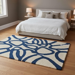 May include: A rectangular area rug featuring a high-pile texture with a bold, abstract pattern of interconnected dark blue organic shapes on a cream-colored background. The rug displays the repeating text A&A CARPETS across its surface.