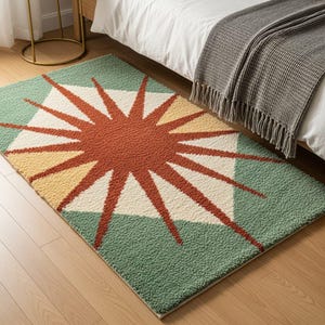 May include: A rectangular area rug featuring a textured, tufted surface with a central sunburst motif in rust orange, cream, and pale yellow. The background consists of sage green geometric shapes, creating a bold, contrasting pattern across the rug.