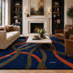 May include: A blue area rug with an abstract design of orange and gray curved lines. The rug is in a living room setting with a sofa, chairs, and a fireplace. The text "AAA CARPETS" is visible on the rug.