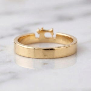 May include: A gold-toned ring featuring a small, detailed silhouette of a sewing machine integrated into the top of the band. The ring has a smooth, polished finish and a consistent, flat-profile band design that encircles the finger.