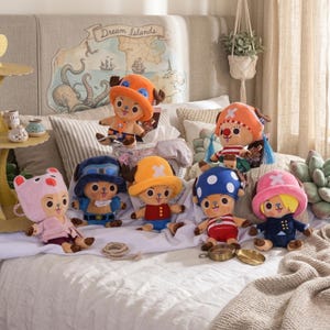 May include: A collection of plush toys featuring a cartoon character with various colored hats and outfits. The toys are arranged on a bed with a map-themed headboard. The hats are in colors like orange, blue, and pink.