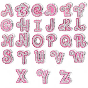 Könnte beinhalten: Eine Sammlung von sechsundzwanzig silberfarbenen Metall-Alphabet-Anhängern, die jeweils mit einer leuchtend rosa Emaille-Einlage und einem Rand aus kleinen, klaren, funkelnden Steinen versehen sind. Jeder Anhänger ist als Buchstabe von A bis Z geformt.