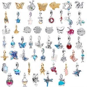 May include: A collection of silver and gold-toned charms with various designs, including butterflies, fish, animals, and abstract shapes. Some charms feature colorful accents like blue, red, and green. These charms are designed to be added to a bracelet or necklace.