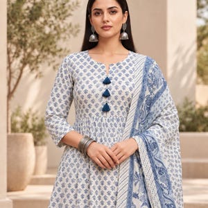 May include: A white and blue patterned cotton dress featuring three-quarter sleeves, a round neckline with three dark blue tassels, and a matching patterned shawl. The garment is accessorised with silver-toned jhumka earrings and silver bangles.