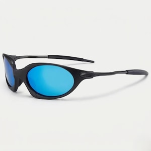 Puede incluir: Gafas de sol negras con lentes azules. Las gafas tienen un dise&ntilde;o elegante y curvado con un acabado mate. Las lentes son de un azul vibrante, contrastando con las monturas negras. Las patillas de las gafas son finas y se extienden hasta las orejeras.