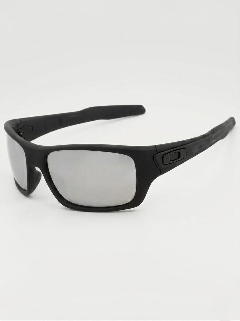 May include: Black sunglasses with silver mirrored lenses. The sunglasses have a matte black frame and a rectangular shape. The arms of the sunglasses are thick and curve slightly. The lenses are reflective.