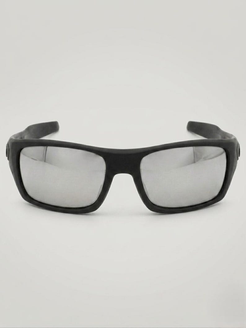 May include: Black sunglasses with rectangular frames and mirrored lenses. The sunglasses have a thick, matte black frame and a sporty design. The lenses reflect light, creating a silver appearance.