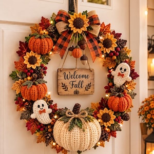 Könnte beinhalten: Ein dekorativer Kranz mit gehäkelten orangefarbenen und cremefarbenen Kürbissen, Sonnenblumen und zwei weißen Geistern mit orangefarbenen Fliegen. Ein Holzschild in der Mitte trägt die Aufschrift Welcome Fall. Der Kranz ist mit Karoband verziert.