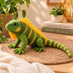 Puede incluir: Un juguete de iguana tejido a ganchillo con cuerpo verde, rayas amarillas y una cresta espinosa amarilla a lo largo de la espalda. El animal de peluche tiene ojos oscuros y una superficie texturizada creada con puntos de lana hechos a mano.