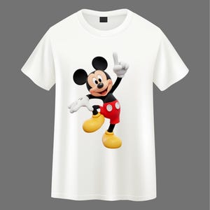 May include: A white short-sleeved t-shirt featuring a centered graphic of Mickey Mouse. The character is depicted in a dynamic pose with one hand raised, wearing red shorts with two white buttons, yellow shoes, and white gloves on a black body.