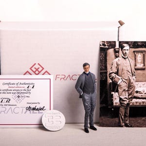 Może przedstawiać: Miniaturowa figurka 3D mężczyzny w garniturze, obok karty kolekcjonerskiej i certyfikatu autentyczności. Karta przedstawia zdjęcie w sepii mężczyzny w garniturze. Obecne są również białe pudełko i srebrna moneta.