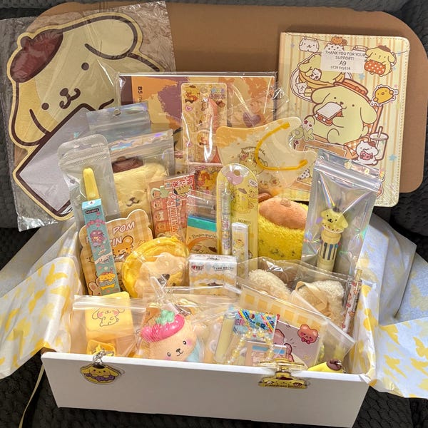 May include: A collection of yellow-themed stationery and accessories featuring the character Pompompurin, including a notebook, pens, pouches, stickers, and small plush items, all packaged together in a white box with yellow patterned tissue paper.