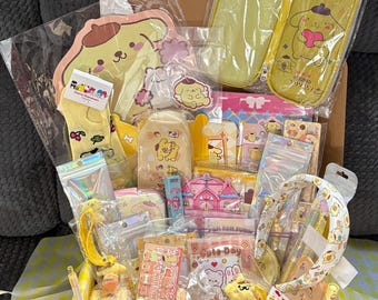 Op de afbeelding: Een verzameling Sanrio-schrijfwaren en accessoires met Pompompurin, waaronder een geel etui, een notitieblok in de vorm van een personage, een haarband, stickers, pennen, een kleine knuffel en diverse verpakte artikelen in een doos.