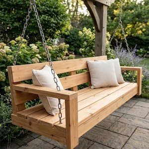 Peut inclure: Un banc-swing en bois avec une finition naturelle, suspendu à des chaînes métalliques. Le banc a une assise et un dossier à lattes, avec deux coussins beiges. Le banc est suspendu à une pergola en bois, entourée de verdure.