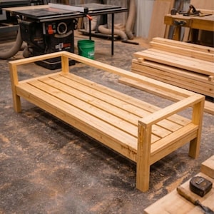 Peut inclure: Un banc en bois clair avec une assise à lattes et un cadre rectangulaire. Le banc est dans un atelier, avec des outils et des matériaux de menuiserie visibles en arrière-plan. Le banc mesure environ 152 cm de long.