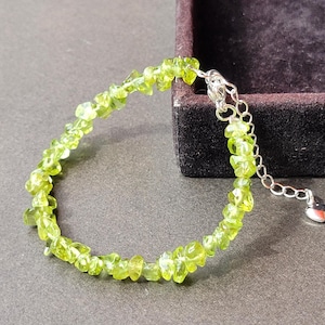 May include: A bracelet composed of small, irregular, translucent lime green peridot chip beads strung together. The bracelet features a silver-toned metal chain extension with a lobster claw clasp and a small heart-shaped charm at the end.