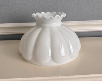 May include: A white milk glass lamp shade featuring a rounded, fluted design with a ruffled top edge. The shade has a smooth, glossy finish and a wide, circular opening at the base, creating a classic dome shape for a light fixture.