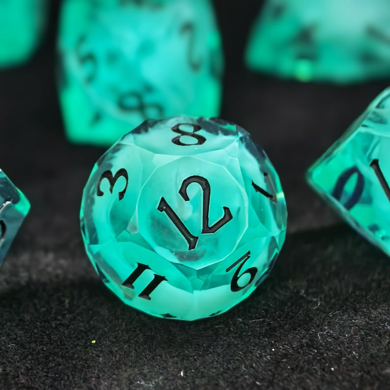 May include: A translucent, bright teal twelve-sided die featuring sharp, faceted edges and bold, black engraved numbers. The die displays the number twelve prominently in the center, surrounded by other visible digits including eight, three, six, and eleven.