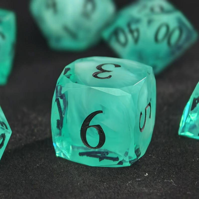 May include: A translucent teal six-sided die with black ink numbers. The die features a swirling internal pattern and sharp edges. The number nine is prominently displayed on the front face, with the number three visible on the top face.