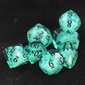 May include: A set of polyhedral dice made from translucent mint green resin with swirling white inclusions inside. Each die features sharp edges and clear black numerical engravings, including a twenty-sided die, a twelve-sided die, and others.