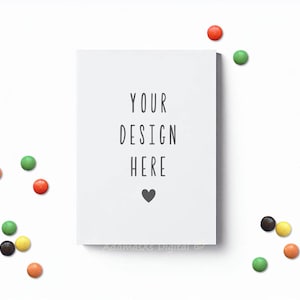 May include: A white card with the text "YOUR DESIGN HERE" and a small black heart. The card is surrounded by colorful candy on a white background.